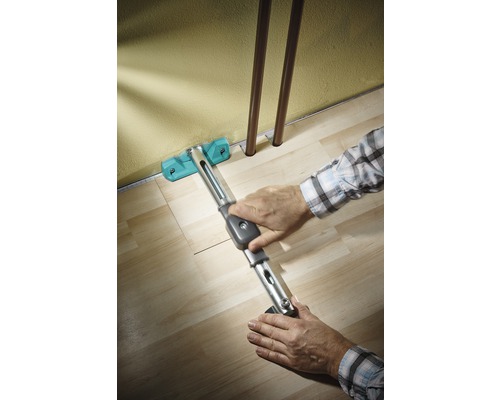 Osoba pokládá laminát pomocí stahováku podél zdi.