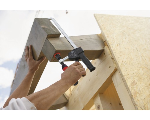 Osoba upevňuje dřevěné trámy ke dřevěnému rámu pomocí svorky.