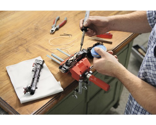 Osoba opravuje model železnice pomocí páječky a šroubové svěrky