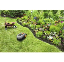 Scéna s robotickou sekačkou, kolečkem, rýčem a květinovým záhonem na zahradě