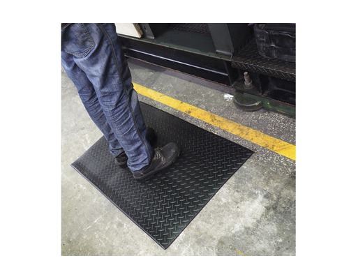 Osoba stojí na protiskluzové podložce v průmyslovém prostředí