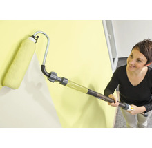 Žena maluje zeď válečkem s nádržkou na barvu