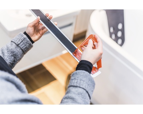 Osoba odstraňuje ochrannou fólii z protiskluzového proužku