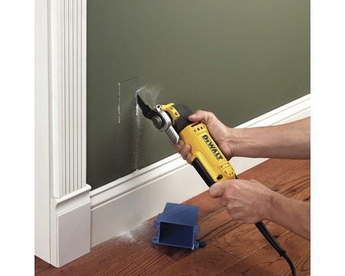 Oscilační elektrické nářadí vyřezává otvor do zelené stěny pro modrou spojovací krabici.