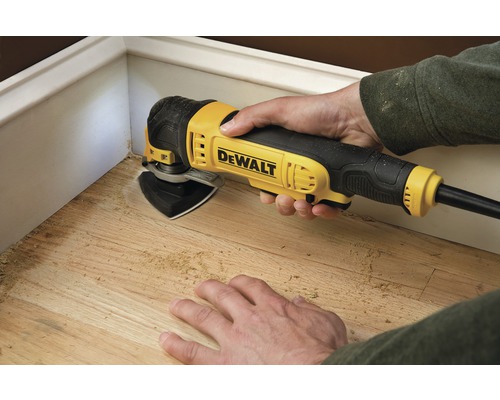 Scéna zobrazuje osobu pracující se dřevem pomocí multifunkčního nástroje značky Dewalt.