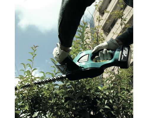 Osoba stříhá živý plot akumulátorovými nůžkami na živý plot.