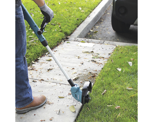 Osoba stříhá okraje trávníku pomocí akumulátorového vyžínače