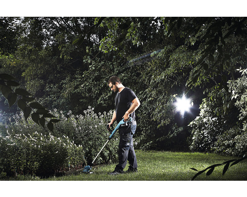 Muž pracuje na zahradě se strunovou sekačkou.