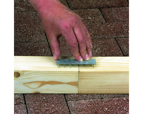 Ruka vtlačuje hřebíkovou desku do kusu dřeva