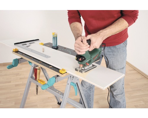 Osoba řeže obrobek přímočarou pilou na pracovním stole.