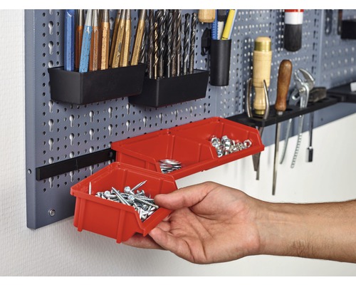 Děrovaná stěna na nářadí s různým nářadím a červenými úložnými boxy
