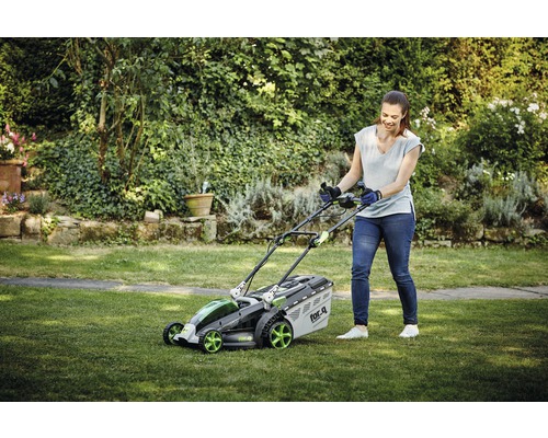 Žena obsluhuje sekačku na trávu na zahradě.
