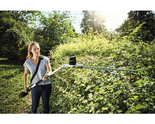 Žena stříhá živý plot pomocí akumulátorových teleskopických nůžek na živý plot