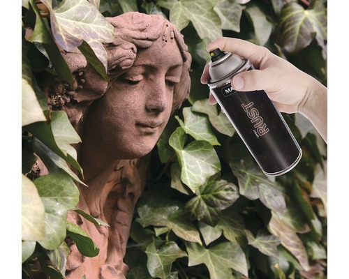 Ruka stříká sprejem s efektem rzi na kamennou sochu před pozadím břečťanu.