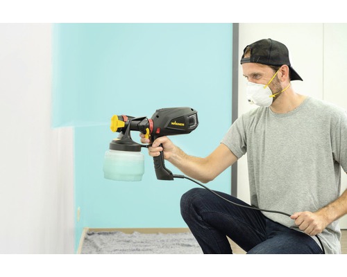 Muž používá stříkací pistoli Wagner k natírání zdi.