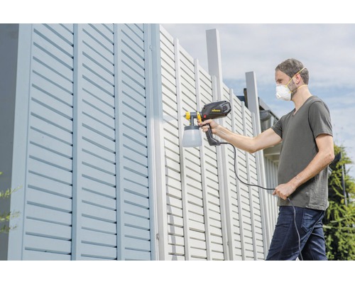 Muž stříká plot pomocí stříkací pistole.