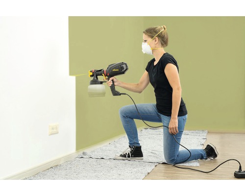 Žena používá stříkací pistoli na malování stěny.