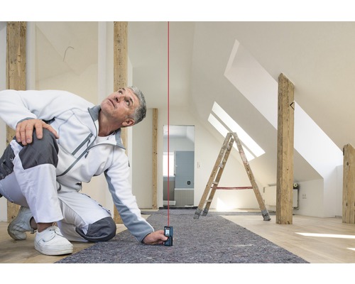 Řemeslník používá laserový dálkoměr v podkroví k provádění přesných měření.