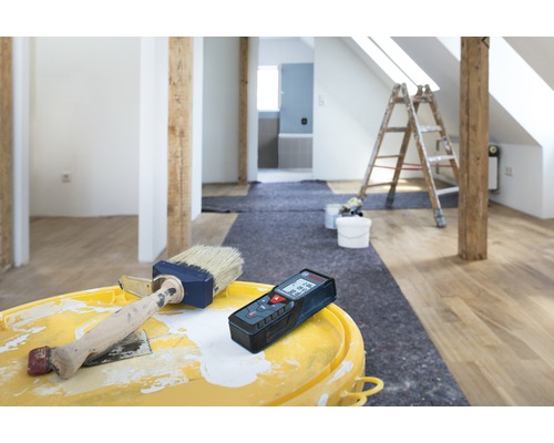 Renovace pokoje s laserovým dálkoměrem, barvou a štětcem na kbelíku