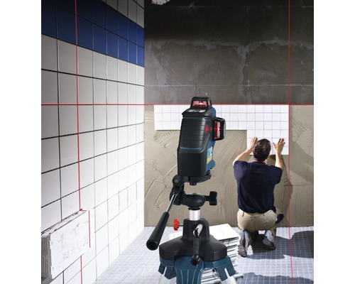 Scéna ukazuje obkladače pracujícího s liniovým laserem pro vyrovnání dlaždic.