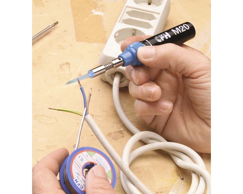 Ruka pájí elektrické vedení páječkou. Na stole leží cívka pájky a zásuvková lišta.