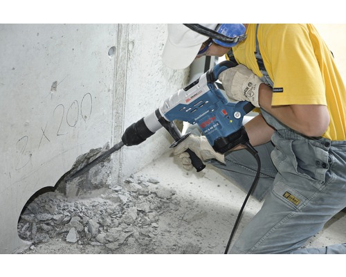 Stavební dělník používá vrtací kladivo k vrtání otvoru do betonové zdi.