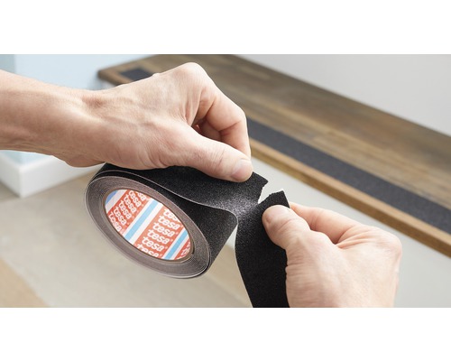 Osoba odřízne kus protiskluzové pásky z role Tesa, aby ji aplikovala na schodiště.