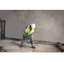 Stavební dělník používá demoliční kladivo k úpravě podlahy.