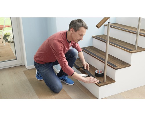 Muž nanáší protiskluzovou pásku na dřevěné schodiště. Role protiskluzové pásky je viditelná.