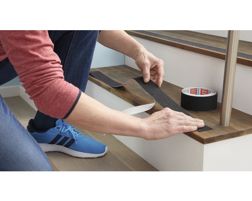 Osoba připevňuje protiskluzovou pásku na schod pro zvýšení bezpečnosti.
