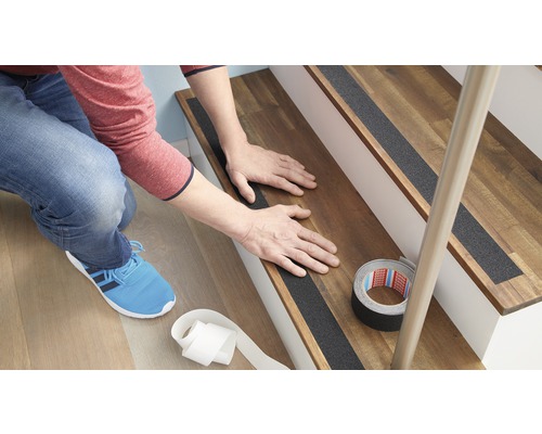 Osoba instaluje protiskluzové pásky na dřevěné schodiště pro zvýšení bezpečnosti.