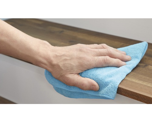 Ruka utírá dřevěný povrch čisticím hadříkem.