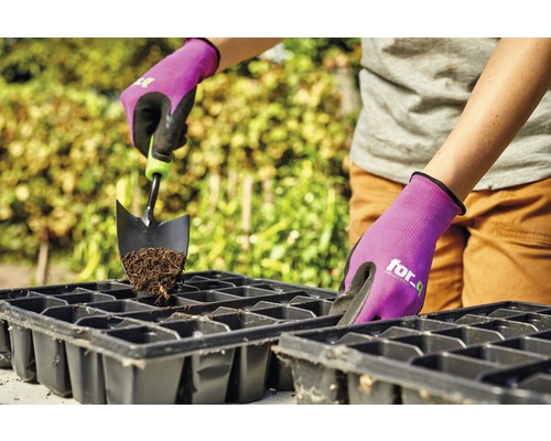 Osoba plní sadbovací misku zeminou a zahradní lopatkou, chráněná zahradními rukavicemi