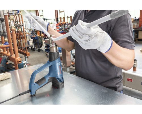 Řemeslník ohýbá plastovou trubku horkovzdušnou pistolí.