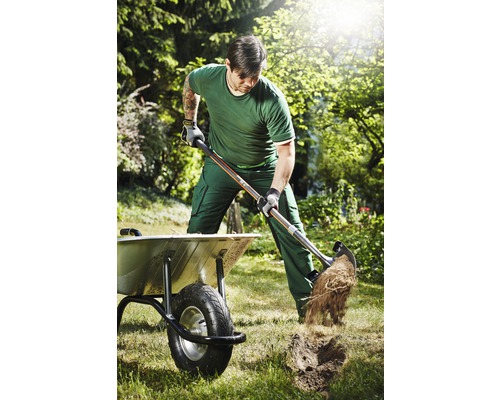 Muž kope rýčem v zahradě vedle kolečka.