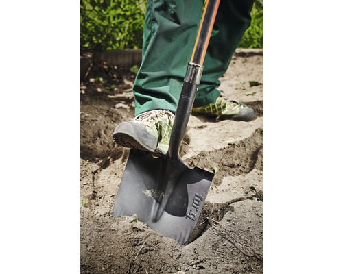 Osoba používá rýč k kopání v zahradě.