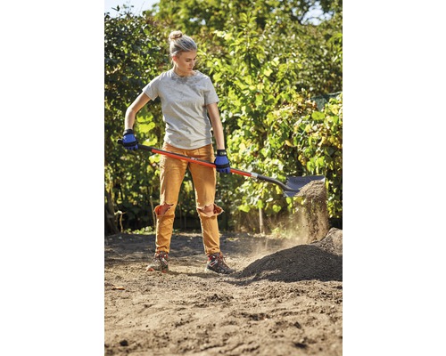 Žena lopatou přehazuje zeminu na zahradě.