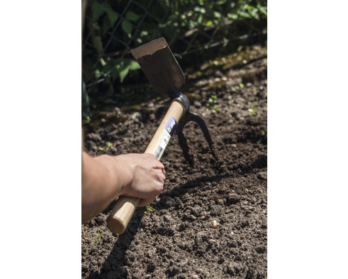 Ruka drží multifunkční motyku v zahradní půdě