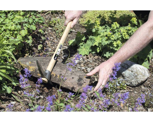 Osoba pracuje na zahradě s motykou s dřevěnou rukojetí.
