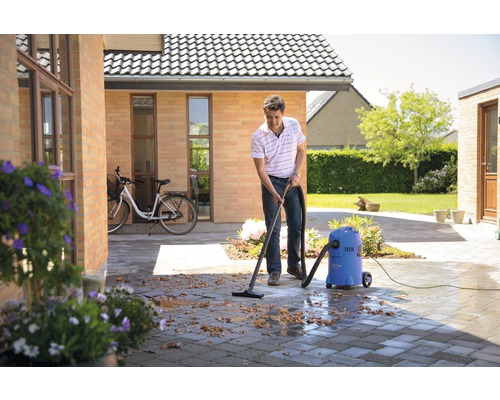 Muž čistí dlažbu venku pomocí mokrého a suchého vysavače.