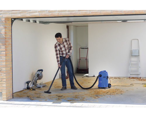 Muž vysává třísky mokro-suchým vysavačem v garáži.