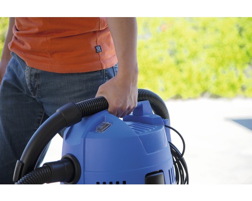 Osoba nese modrý víceúčelový vysavač s hadicí.