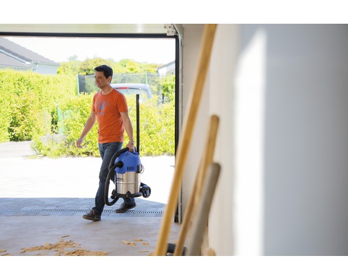 Muž nese mokrý suchý vysavač v garáži.