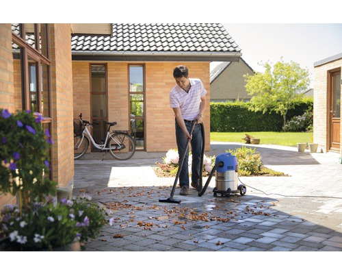 Muž čistí mokrým a suchým vysavačem dlážděnou venkovní plochu od listí.