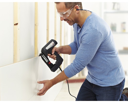 Muž připevňuje nástěnné panely ke zdi pomocí elektrické sponkovačky.
