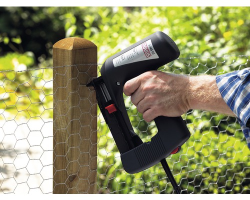 Osoba připevňuje pletivo k dřevěnému sloupku pomocí elektrické sponkovačky.