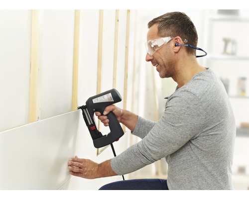 Muž připevňuje stěnové panely k elektrické sešívačce na stěnu