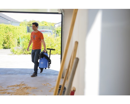 Muž vynáší mokrý a suchý vysavač z garáže.