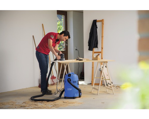 Muž brousí dřevo bruskou vedle vysavače v dílně