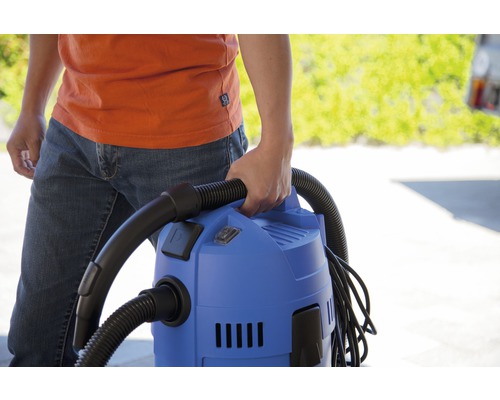 Osoba drží modrý víceúčelový vysavač s černou hadicí.